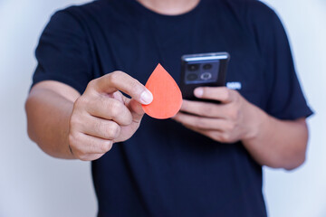 A person holds a red paper droplet while using a smartphone, symbolizing health awareness.
