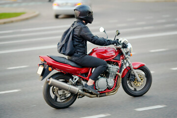 Fototapeta premium Man on red motorcycle cruising down city road, thrill of city riding and the lifestyle of motorcyclist. Motorcyclist in protective helmet on motorbike riding. Selective focus, motion blur