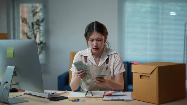 Stressed asian woman entrepreneur getting frustrated and having headache while counting money at her startup home office