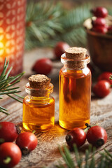Two bottles of rose hip seed oil with fresh rosehips, candle and spruce branches