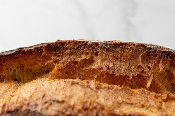 This image showcases a freshly baked, crispy golden bread loaf on a pristine marble kitchen surface, highlighting the texture and artisanal quality of the bread.
