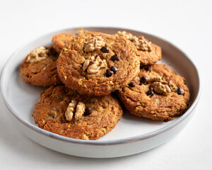 A pile of vegan oatmeal cookies with chocolate chips and walnuts, featuring a clean white backdrop, ai.