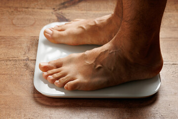 Man legs stepping on floor scales, close-up, bare feet standing on scales, white background. Diet and overweight concept