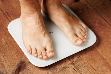 Man legs stepping on floor scales, close-up, bare feet standing on scales, white background. Diet and overweight concept