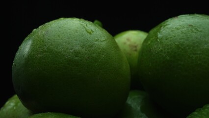 Slices of lime are meticulously arranged in a pile, set against a black background. Each lime slice is captured in stunning detail, its vibrant green hue and enticing texture. Close up. Comestible.