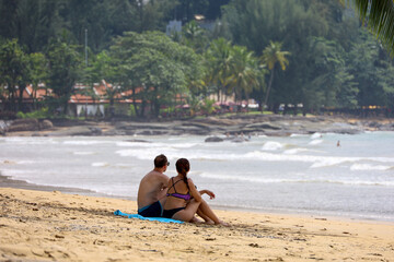 Couple in swimwear sitting on the sand of tropical beach. Holidays on sea coast