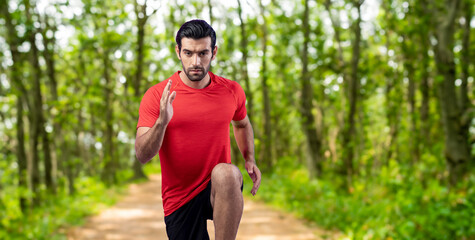 Fototapeta premium Athletic and sporty man running posture at outdoor green forest exercise session for fit physique and healthy outdoor sport lifestyle. Gaiety green foliage tree exercise workout training.