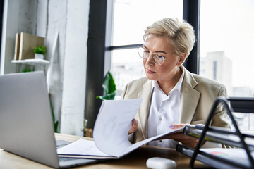 A fashionable woman attentively examines papers while seated at her modern desk.