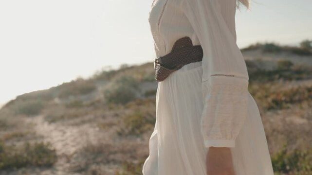 A seductive slow motion shot of a woman in a flowing white dress walking on the beach.