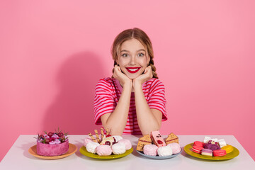Young girl with charming smile surrounded by colorful desserts, in a casually fashionable striped t-shirt, and vibrant red lipstick.