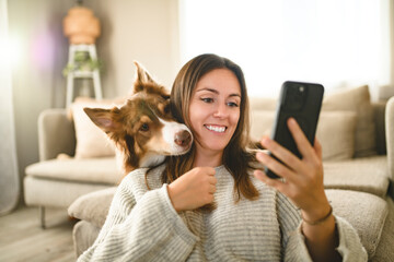 woman with cute fluffy Australian Shepherd dog at home using cellphone in living room