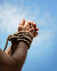 Rope tied hands on sky background