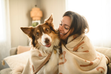 woman with cute fluffy Australian Shepherd dog at home under blanket in living room