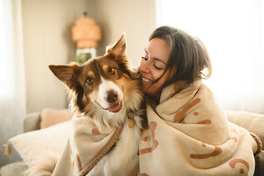 woman with cute fluffy Australian Shepherd dog at home under blanket in living room