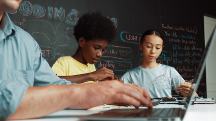 Young student fixing controller while teacher programing engineering code at STEM class. Closeup of...