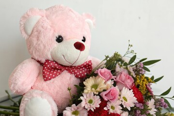 Soft pink heart-shaped bear with white fur, wearing a red bow tie, sitting on a floral bouquet, bow ties, plush toys, valentines day gift