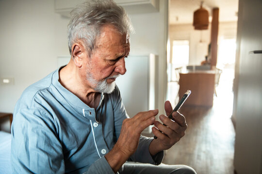 Senior man talking on the smartphone holding chest at home