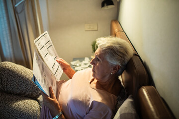 Worried senior woman reading bills in bed at night