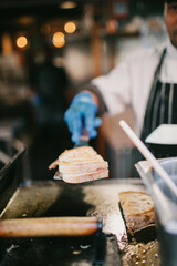 Hand in a blue glove holding hot toasty sandwich on a street food market