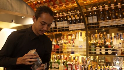 Smiling Asian smart bartender shaking with two hands in mixed cocktail in shaker preparing at luxurious counter bar, preparation special refreshment alcohol drink nightlife warm nightclub. Vinosity.