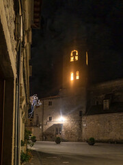 Quiet night scene in a historic plaza with illuminated bell tower and stone buildings.