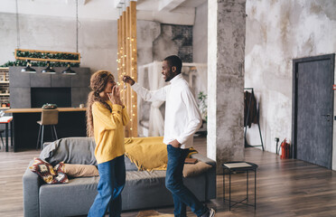 Fototapeta premium Excited couple celebrates new home, with dark-skinned man giving keys to his surprised partner in a cozy, modern living room. Joyful moment highlights love, commitment, and shared dreams