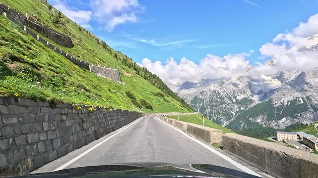 Stunning view from car driving along the winding Stelvio Pass, high in the mountains. Alpine peaks rise majestically, some hidden in clouds, creating breathtaking and dramatic landscape.