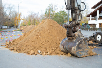 Construction equipment digs earthen trench. excavator with bucket near a mound of dirt. excavation work on a construction site on a road