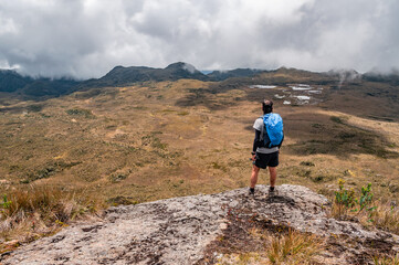 Fototapeta premium man looking at a group of lagoons between mountains full of vegetation in the depth of the Colombian landscape with a blue cap enjoying a free lifestyle