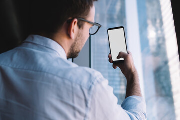 Back view of male employer photographing images during work day, formally dressed businessman using cellphone camera for clicking pictures via mobile medial application with mock up blank screen
