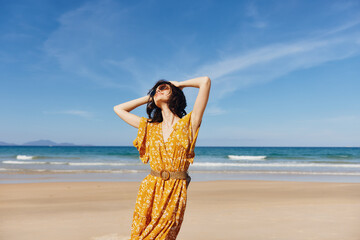 Beautiful woman in yellow dress standing on sandy beach with hands on head on a sunny day