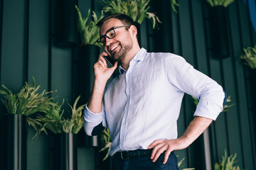 Cheerful manager speaking on smartphone near wall with plants