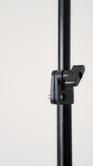 A close-up of a black metal pole with a plastic clamp attached. The clamp has a lever that can be tightened to secure an object to the pole