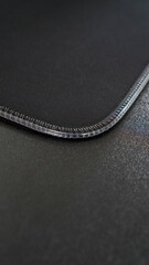 A close-up of a black mouse pad with a stitched edge. The pad has a smooth, matte surface designed for precise mouse movement. The stitched edge provides a durable and professional finish. © AbiezaReswara