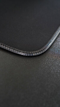 A close-up of a black mouse pad with a stitched edge. The pad has a smooth, matte surface designed for precise mouse movement. The stitched edge provides a durable and professional finish.