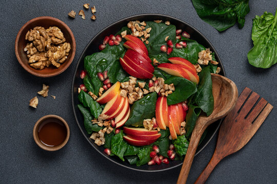Seasonal salad with pomegranate seeds, walnuts, apples and spinach in a black plate on a dark background, top view