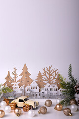 A delightful vintage toy car in cream, paired with golden gift boxes adorned with bows, rests on a white backdrop, complemented by tiny pine branches and a pine cone for a festive touch.