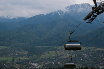 Obraz premium Ski Lift snowy mountain autumn forest with chair lift At The Ski Resort in Zakopane Poland. Holidays Vacation sport and outdoor activities tourism cable car empty seat grass field in green forest on