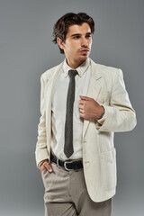 A young man in stylish formal wear poses gracefully against a sleek grey backdrop, exuding charisma.
