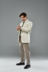 A young, handsome man dressed in formal attire intently checks his wristwatch while posing in a studio.