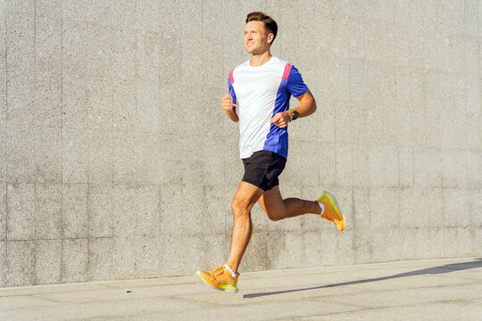 A Young Man Jogging Along a Concrete Path on a Sunny Day, Wearing Athletic Gear and Enjoying Exercise