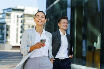 Professionals Walking Outside Modern Office Building, Using Smartphones During a Sunny Day in the City