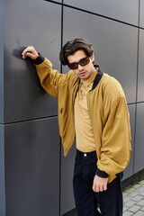 A young handsome man showcases his fashionable autumn look while leaning against a contemporary wall.