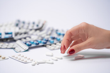 Close up image of young female hand taking white round pill from table, lots of pharmaceutical pills and capsules, colorful medicine pills in background.