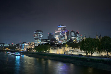Nighttime view of London's skyline featuring skyscrapers and the historic Tower of London along the River Thames