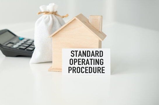 Standard Operating Procedure text written on a card with a figure of a wooden house and a calculator on a light table.
