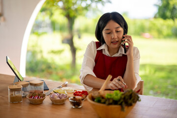 Asian woman cooking healthy food and using smartphone at the same time in a modern kitchen