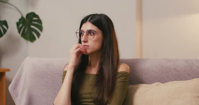 Young woman in glasses contemplates with concern touching chin