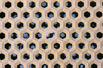 Metal sewer lid with signs of rust and weathering. Hexagon shaped metal combs. Structure is reflected in the water below the lid.