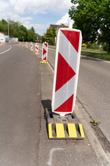 Row of reflective traffic diversion signs in red and white with yellow stands. Daytime scene, blue dky with white clouds.